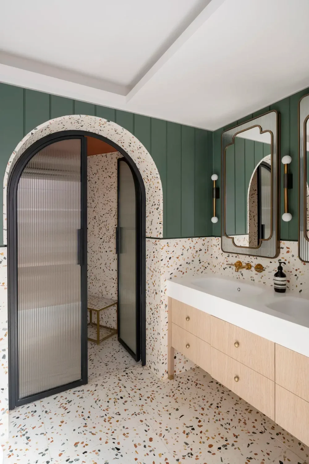 bathroom-green-walls-terrazzo-tiles-double-sink-arched-ribbed-glass-doors-nordroom