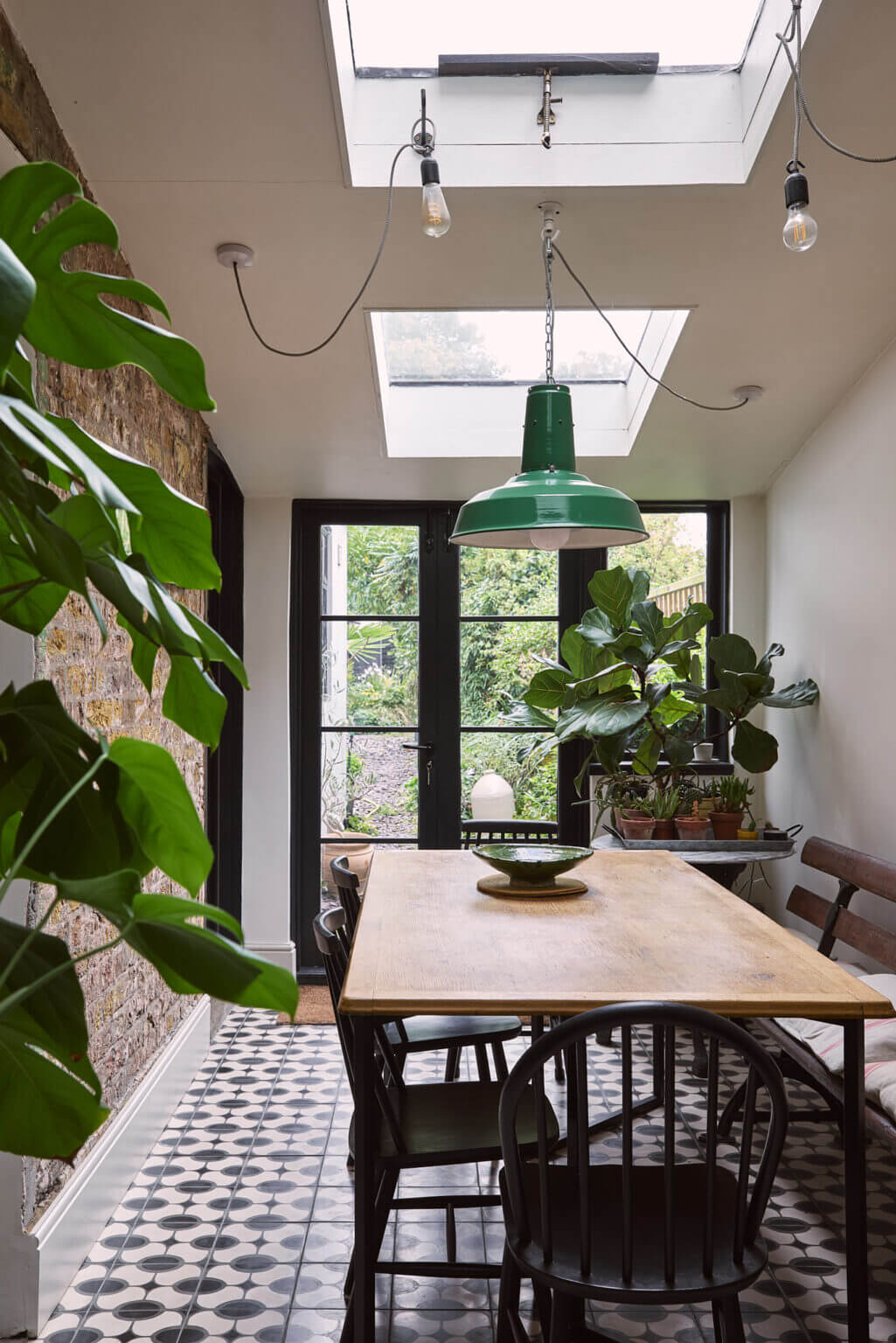 dining room with tiled floor green pendant skylights and brick wall