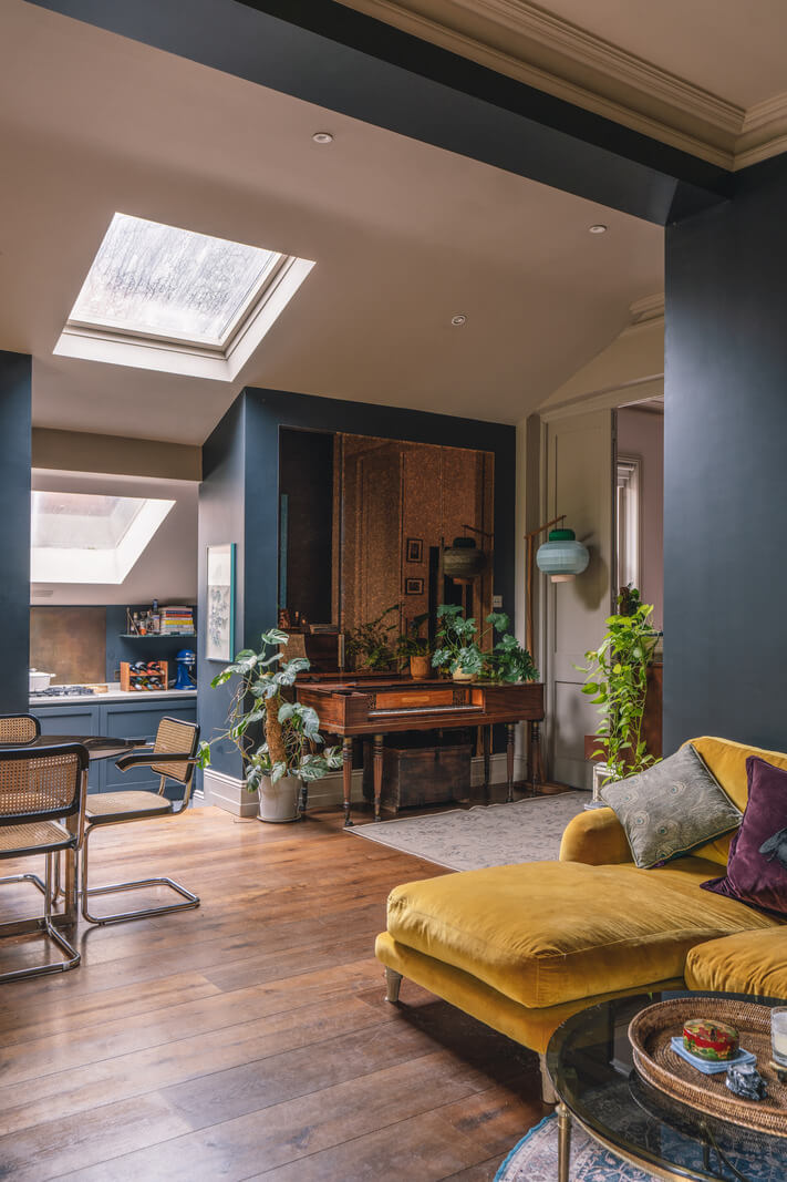 open plan living space with dark blue walls pitched ceiling and ochre couch nordroom