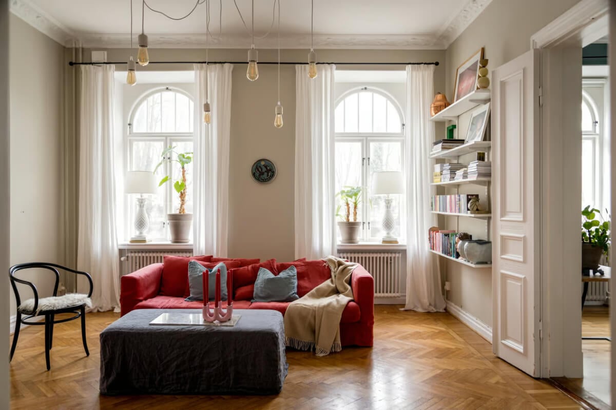 Large Rooms in an Art Nouveau Apartment in Sweden 2 living room with arched windows parquet floor and red sofa