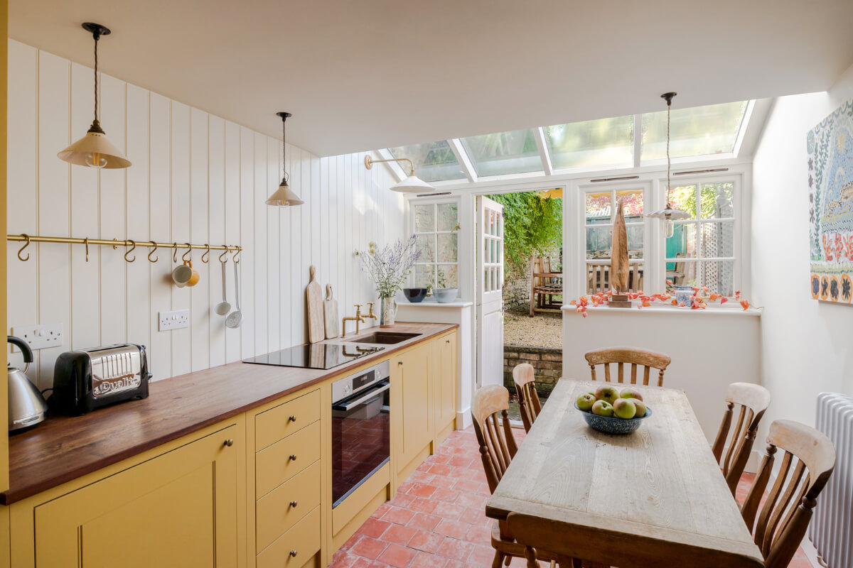 ochre yellow kitchen with brass fittings stone floor and wooden table