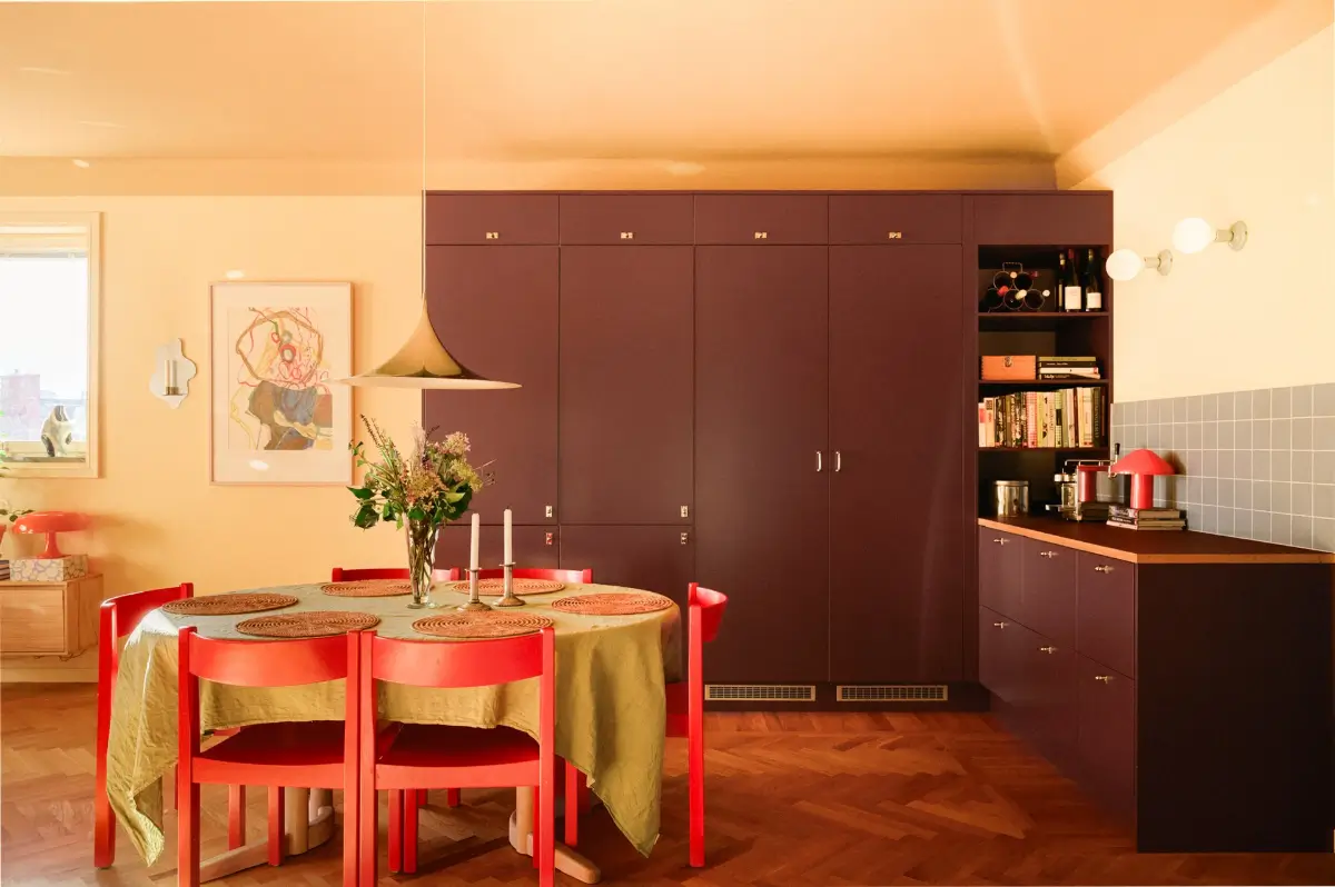 A Colorful Stockholm Family Apartment with Views of the Lake 9 plum-colored kitchen cabinets dining table green tablecloth red chairs nordroom